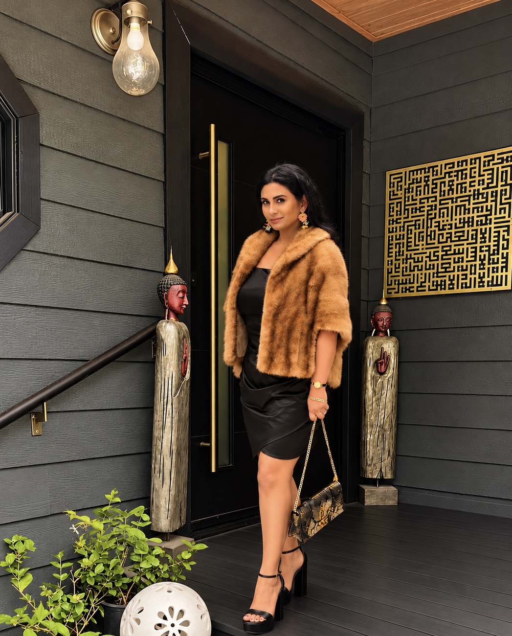 Anabin Islam, founder of Final Cut Advisory, in a mink stole and black satin dress, stepping out of a black front door flanked by carved Buddha figures and a gold calligraphy panel