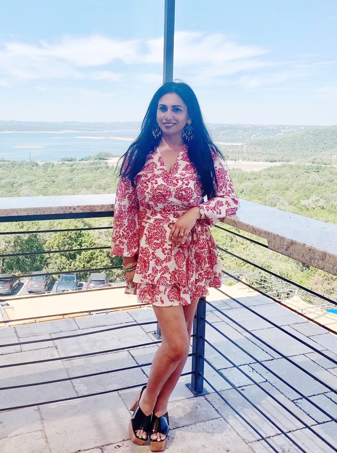 Founder in a red and white print wrap romper on a terrace overlooking the lake and hills